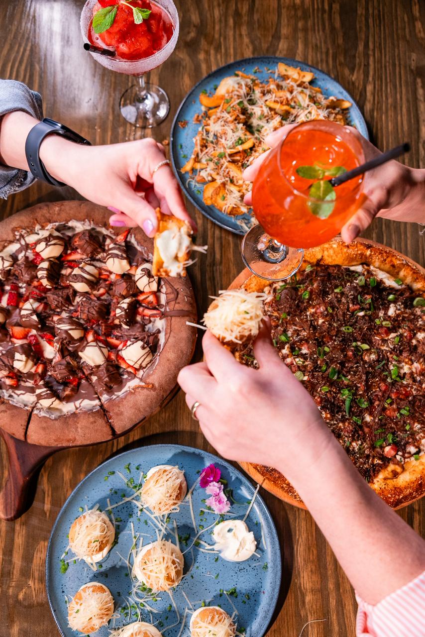 Mesa com pizzas, bolinhos de queijo, drinks e sobremesas do The Family's